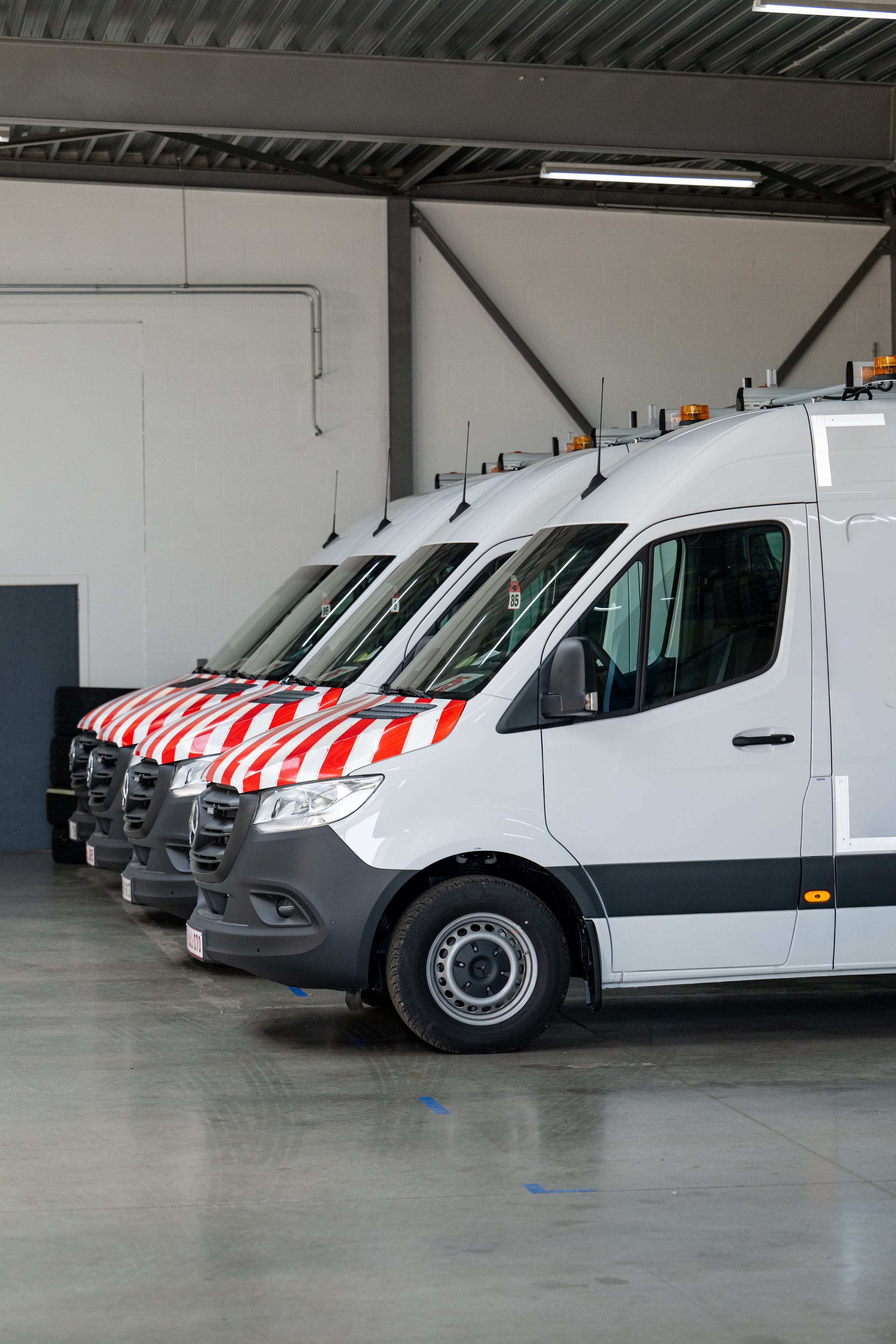 Flotte de Mercedes Sprinter avec galeries de toit et marquage de signalisation rouge et blanc dans l’atelier Amecam